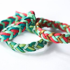 May include: Three braided leather bracelets in green, red, and gold. The bracelets are woven together in a complex pattern.