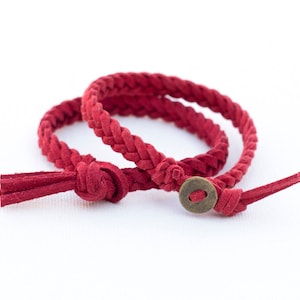 May include: Two red braided leather bracelets with a small brass button closure.