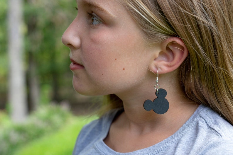 May include: A young person wearing black Mickey Mouse earrings. The earrings are made of black felt and have silver hooks.