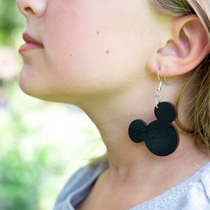 May include: A pair of black wooden earrings shaped like Mickey Mouse heads. The earrings are hanging from silver hooks.