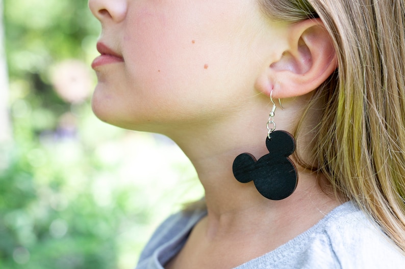 May include: A pair of black wooden earrings shaped like Mickey Mouse heads. The earrings are hanging from silver hooks.