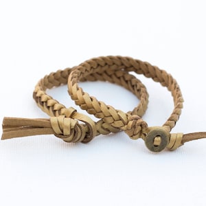 Puede incluir: Dos pulseras trenzadas de cuero marrón con cierre de botón de latón.