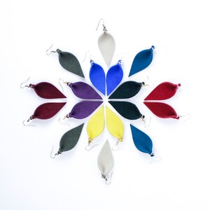 Puede incluir: Un conjunto de diez pendientes de fieltro en varios colores, incluyendo azul, rojo, amarillo, verde y morado. Los pendientes tienen forma de lágrima y están dispuestos en un patrón circular.