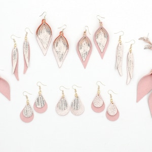 Può includere: Assortimento di orecchini in pelle rosa e oro. Gli orecchini sono di varie forme, tra cui a goccia, a piuma e a foglia.