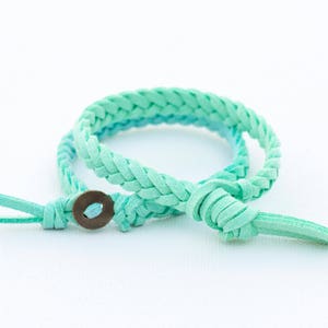 Könnte beinhalten: Ein geflochtenes türkisfarbenes Lederarmband mit einem Metallknopfverschluss.