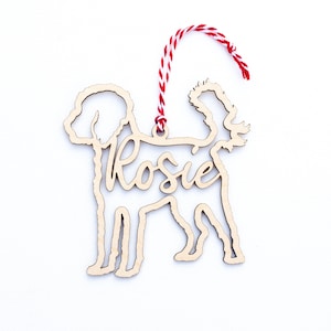 Può includere: Ciondolo in legno a forma di cane con il nome "Rosie" ritagliato. Il ciondolo è attaccato a uno spago rosso e bianco.