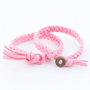 May include: Two pink braided leather bracelets with a tassel and a metal button closure.