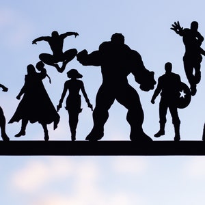 Peut inclure: Silhouettes de personnages de super-héros populaires, dont Hulk, Spiderman, Black Panther, Captain America, et plus encore, découpées dans du métal noir et disposées sur une barre en métal noir.