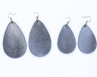 May include: Four pairs of teardrop-shaped earrings made of gray leather. The earrings are all the same shape, but they vary in size. The earrings are hanging from silver hooks.