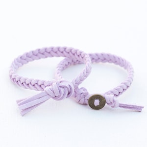 May include: Two lavender braided leather bracelets with a metal button closure. One bracelet has a tassel.