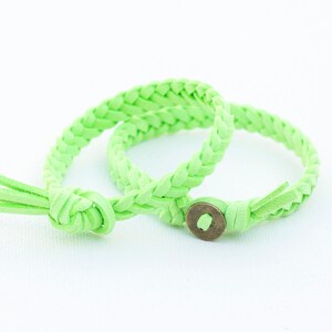 May include: Two green braided leather bracelets with a metal clasp. The bracelets are tied together in a knot.