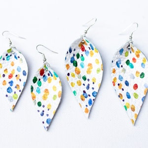 May include: Three pairs of white leather earrings with a colourful confetti pattern. The earrings are shaped like a teardrop and have silver hooks.