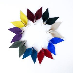 May include: A set of 10 pairs of felt earrings in various colours, including yellow, purple, green, blue, and red. The earrings are shaped like teardrops and are arranged in a circle on a white background.