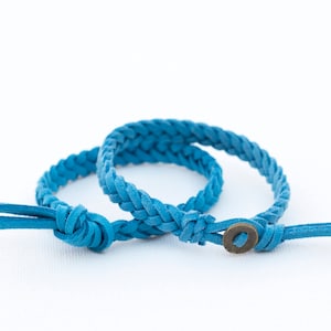 May include: Two blue leather braided bracelets with a metal button closure.