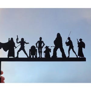 Puede incluir: Siluetas negras recortadas de personajes de Star Wars, incluyendo Darth Vader, Luke Skywalker, Yoda, Chewbacca, R2-D2 y otros, montadas en un marco de metal negro.