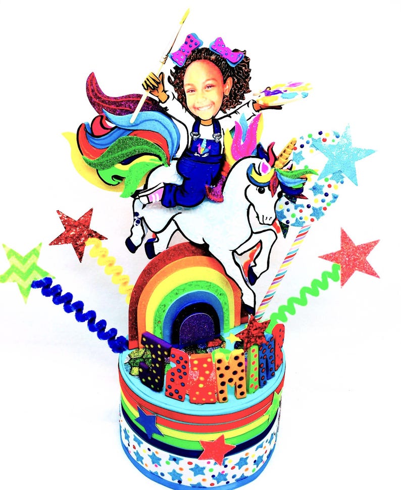 May include: A vibrant birthday cake with a unicorn theme. The cake features a cartoon girl riding a white unicorn over a rainbow. The cake is decorated with stars, the name "SAMI", and colorful layers.