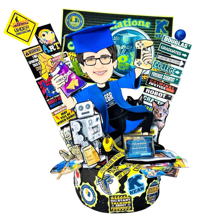K&ouml;nnte beinhalten: Ein Tortenaufleger zum Thema Abschlussfeier mit einer Karikatur eines Absolventen in blauem Talar, der einen Gamecontroller und eine T&uuml;te Chips h&auml;lt. Der Sockel ist mit verschiedenen Schildern, einem Roboter, einem Laptop und einer Katze verziert.