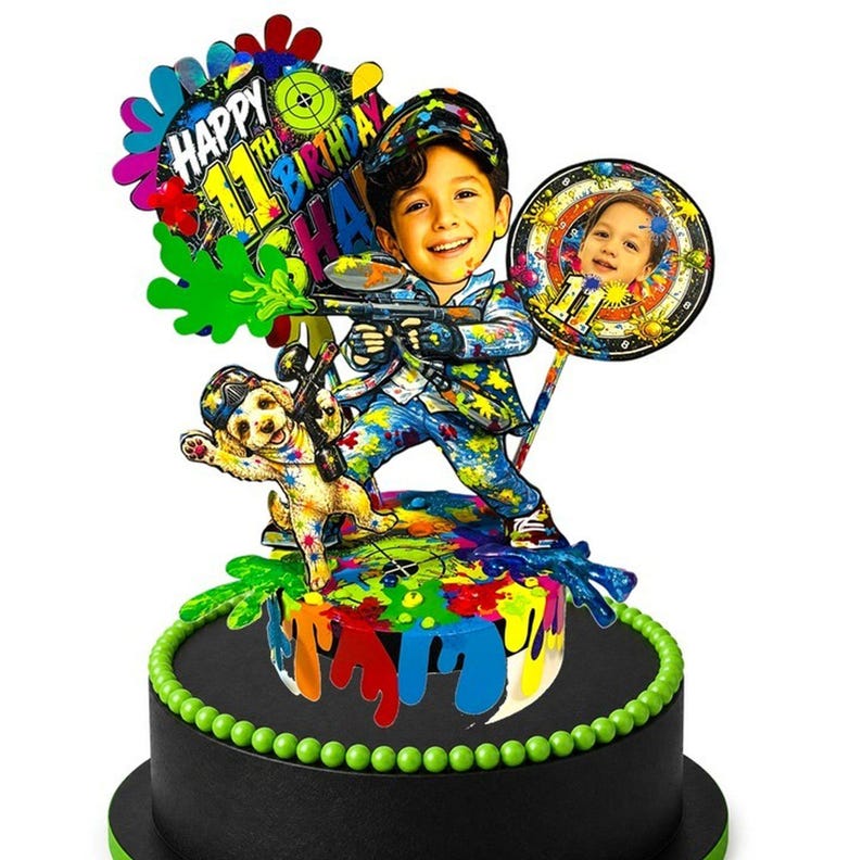 May include: A multi-layered cake topper featuring a cartoon illustration of a child holding a paintball gun, a puppy, and a circular photo cutout. The design includes vibrant paint splatters, a target icon, and text reading Happy 11th Birthday.