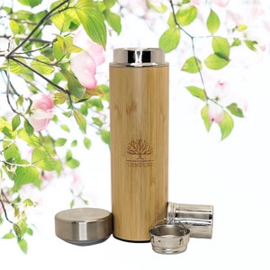 May include: A bamboo travel mug with a stainless steel lid and infuser. The mug has a natural wood grain finish and features the word "UENDURE" with a tree logo. The lid and infuser are detached, and the background has pink flowers and green leaves.
