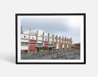 May include: A digital illustration of Bramall Lane, the home of Sheffield United Football Club. The stadium is depicted in a cartoon style with a crowd of fans in front of the entrance. The sign above the entrance reads "Welcome to Bramall Lane".
