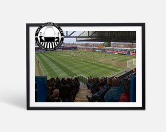 May include: A black and white illustration of a football stadium with the text "Luke Williamson Art The Football Ground Collection" in a circle. The image shows a view from the stands of a football match in progress.