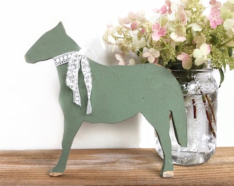 May include: A green wooden horse figurine with a white lace ribbon around its neck. The horse is standing on a wooden surface next to a glass vase filled with pink and white flowers.