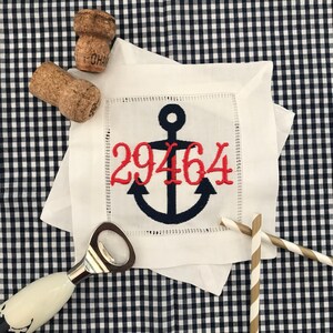 May include: White linen cocktail napkin with a blue anchor and red embroidered numbers "29464".