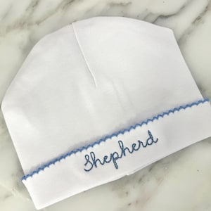 May include: White baby hat with a blue scalloped trim and the word "Shepherd" embroidered in blue.