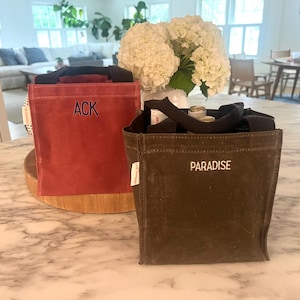 Puede incluir: Dos bolsas de lona con bordado personalizado. La bolsa roja dice "ACK" y la bolsa marrón dice "PARADISE".