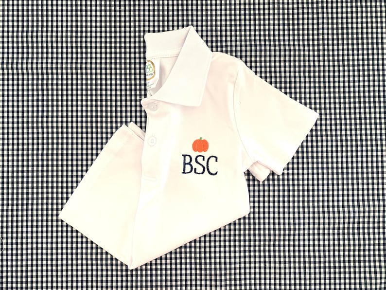 May include: White short-sleeved polo shirt with an embroidered pumpkin and the initials "BSC" in navy blue.