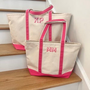 May include: Two canvas tote bags with pink handles and trim. The larger bag has the initials "KP" embroidered on the front. The smaller bag has the initials "MM" embroidered on the front.