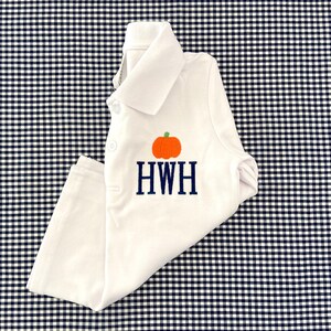 May include: White baby onesie with a pumpkin and the monogram HWH embroidered on the front. The onesie is lying on a black and white gingham fabric.