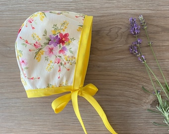 May include: A yellow bonnet with a floral print and yellow ties. The bonnet is made of a soft, lightweight fabric and is perfect for keeping a baby's head warm and protected from the sun.