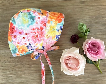 May include: A floral print bonnet with a gathered crown and two long ties. The bonnet is made of a lightweight fabric and features a variety of colorful flowers.