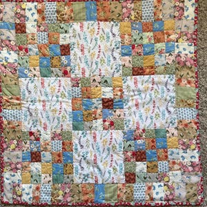 May include: A patchwork quilt featuring floral and geometric designs in blue, green, yellow, and pink. The quilt has a red border and is constructed from fabric squares.