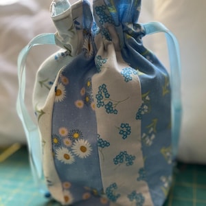 May include: A blue and white drawstring bag with a floral pattern. The bag has blue ribbon ties.