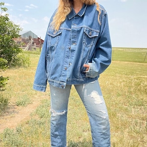 May include: A blue denim jacket with a button-up front and long sleeves. The jacket is oversized and has a relaxed fit.
