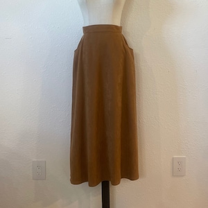 May include: A brown midi skirt with a high waist and pockets. The skirt is made of a smooth, slightly textured fabric.