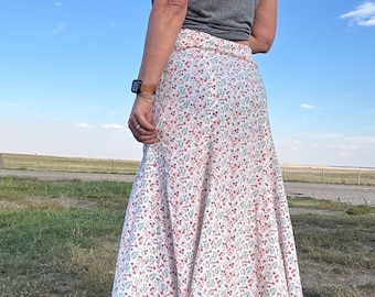 May include: A white skirt with a floral print in shades of pink, blue, and green. The skirt is knee-length and has a flowy, A-line silhouette.