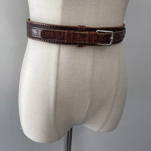 May include: A brown leather belt with an intricate floral design and a silver buckle.
