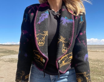 May include: A black cropped jacket with a colorful southwestern pattern featuring animals and geometric designs. The jacket has a pink trim and a zipper closure.