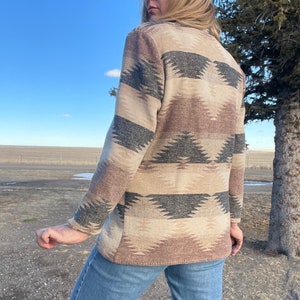 Może przedstawiać: Długi kardigan z geometrycznym wzorem w odcieniach brązu, beżu i czerni. Kardigan wykonany jest z miękkiej, fakturowanej tkaniny.