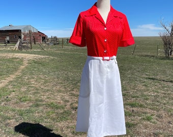 Puede incluir: Una falda blanca con una blusa de lunares rojos y blancos. La falda tiene un cinturón y bolsillos. La blusa tiene mangas cortas y un cuello.