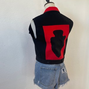 May include: A black denim vest with a red panel on the back. The panel features a black silhouette of an arrowhead.