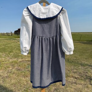 May include: A white collared dress with a blue and white houndstooth pattern. The dress has a white collar and long sleeves.