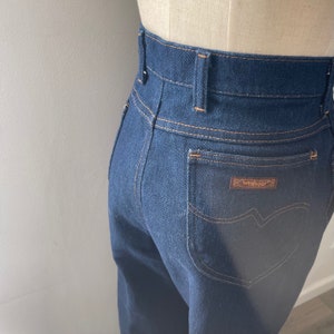May include: Dark blue denim jeans with a high waist and a back pocket with a brown leather Wrangler label.