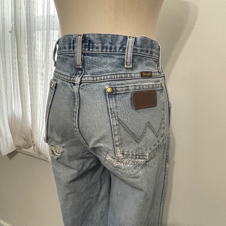 May include: Light blue denim jeans with a brown leather patch on the back pocket. The jeans have a distressed look with some rips and tears.