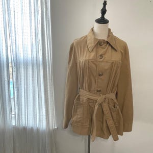 May include: A brown corduroy jacket with a button-up front, a belt, and two large pockets. The jacket has a pleated design on the front.