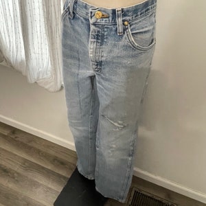May include: Light blue denim jeans with a distressed look and a gold button.
