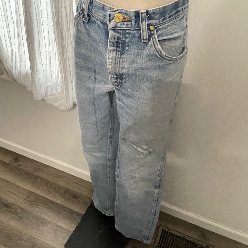 May include: Light blue denim jeans with a distressed look and a gold button.